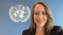 Woman wearing a black suit standing in front of a blue wall with the UN logo