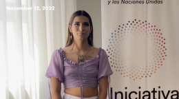 Person in a purple dress standing in front of a white background with the Spotlight Initiative logo.
