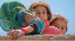 Three Afghan girls in blue dress, pink dress, hidden behind a wall