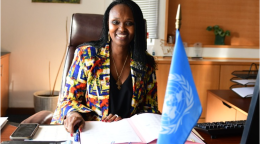 Femme dans une chemise colorée assise à un bureau avec un drapeau de l'ONU