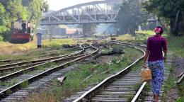 A woman in a purple top walks along a railroad on a sunny day. 