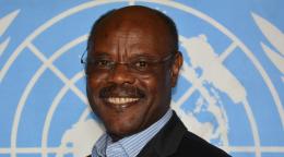 man in dark suit stands in front of UN flag 