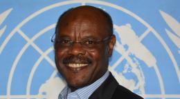 man in dark suit stands in front of UN flag 