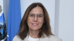 Woman in a white suit with glasses standing in front of a united nations blue coloured flag