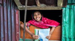 Girl in a pink dress holding a book peeping through a window