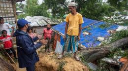 Group of people including two children gather around some rubble and blue tarpaulin