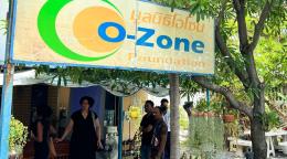 A bright yellow billboard saying "Ozone" underneath which a group of people are gathered