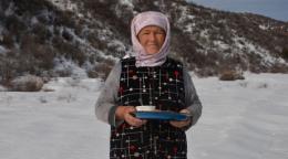 A Kyrgyz woman in a black dress and woollen headscarf holds a piece of ice