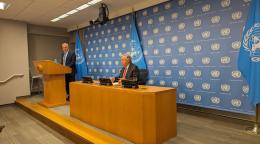 A UN official (the head of the UN) speaks to press from a small stage with a podium and microphone.