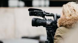 Фотография женщины, блондинки, со спины, которая стоит рядом с видео камерой