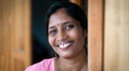 A woman in a light pink shirt smiles next to a door frame.