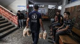 A WFP humanitarian worker in a black shirt carries bags of grain into a UNWRA school in Gaza where communities are seeking refuge.