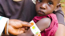 A baby is being held with a mid-upper arm circumference to help determine malnutrition.