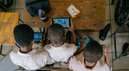 An aerial shot of three children cover over a screen in a school