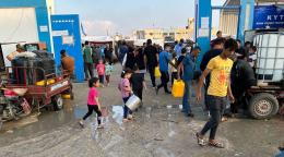 People walk around what looks like a crowded market on muddy ground. 