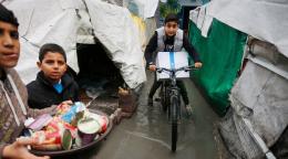 A picture of three children, one of them is on a bicycle, two of them hold baskets of food assistance