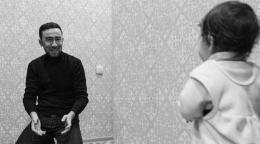 Отец сидит на стуле и с улыбкой общается с маленьким ребенком