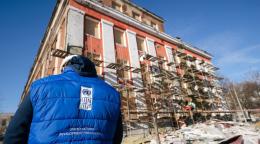 The back of a person in a blue jacket and cap standing in front of a building under construction in Ukraine