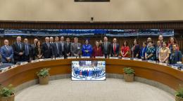 A group of UN officials stand in a semi-circle, and pose and smile for a group photo.