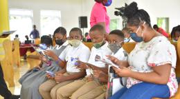 A row of schoolchildren in uniforms sit and read through books