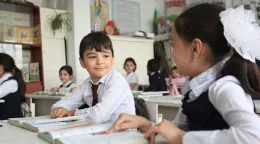 A classroom setting where a boy in a white school uniform smiles at a girl in a blue pinafore