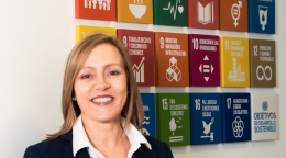Une femme en costume sombre se tient devant un mur avec des panneaux colorés illustrant les objectifs de développement durable.