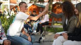 A boy in a white shirt gives a high five to a woman in a dark shirt while others look on, in a school playground.