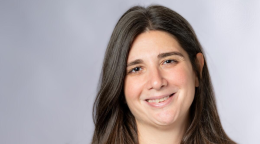 A woman in dark brown hair smiles to the camera