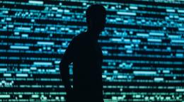 A silhouette of a man against a screen with code written all over it