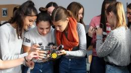 A group of girls huddle around each other as they examine some mechanical parts for a robot.