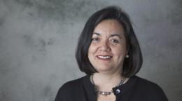 A woman in a black shirt and silver necklace with a bob hairstyle smiles into the camera.