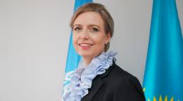 A headshot of a woman in a black suit blazer and blue scarf