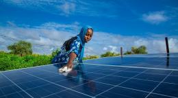 A woman in a blue dress wipes down a solar panel in Africa