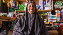 A woman is looking at the camera and smiling and behind her is a shop front