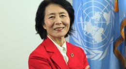A woman in a red suit blazer against a blue UN flag
