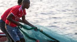Two young men are on a boat in the water fishing with a net