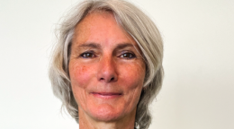 A woman in a green shirt stands in front of a white wall.