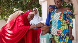 A woman in Nigeria administers a vaccine to a young girl in front of other women.
