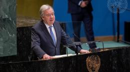 A man inn a dark grey suit and blue tie, the UN Secretary-General, speaks from a podium at the UN building