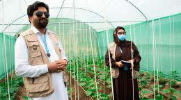 An Afghani man and woman stand in a micro greenhouse.