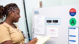A health worker in Trinidad and Tobago takes notes in front of a vaccine storage refrigerator.