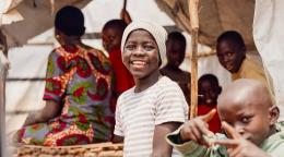 A young boy in Burundi smiles for a photo while surrounded by friends and siblings.