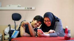 A boy and his mother laugh while watching something on her phone.