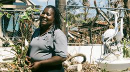 A woman in Jamaica stands in front of destruction brought on by a hurricane.