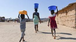A woman in Angola walks with a bucket of water on her head, followed by her son and daughter, also carrying buckets.