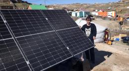 Женщина стоит у солнечной панели на фоне юрточного района города.