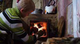 A boy in Ukraine puts firewood in a wood heater.