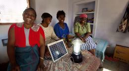 Four women stand around a solar panel.