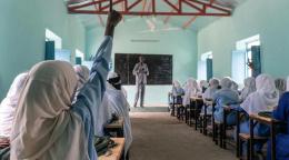 Female students raise their hands in a classroom in Sudan. 