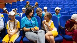 Майя сидит на кресле и разговаривает с девочкой, которая с интересом её слушает.